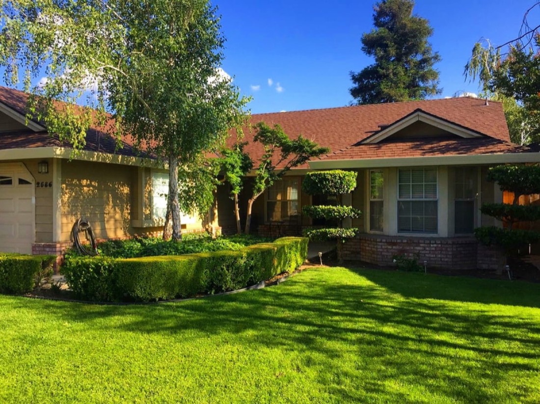 Central Valley ranch home flanked by mature trees — the typical Stanislaus County roof exposed to wind, falling-limb, and storm peril a homeowner's policy covers