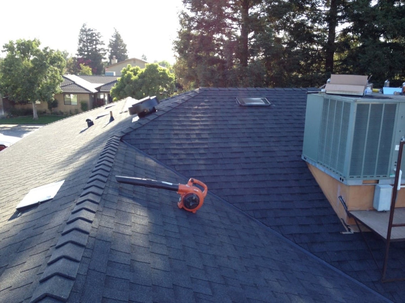 Close-up of a Central Valley roof showing ridge cap detail and HVAC condenser — cost factors for metal vs. shingle pricing
