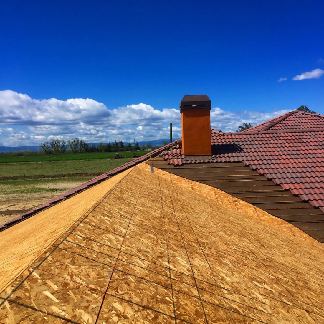 DeHart Roofing crew mid-install on a rural Stanislaus County tile roof — new OSB decking down, original tile retained