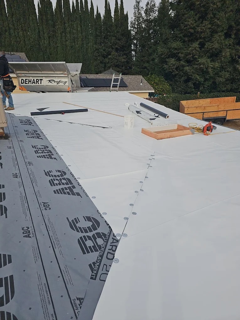 DeHart Roofing crew installing white TPO membrane on a residential flat roof